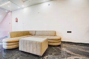 A modern interior with a beige sectional sofa, a glass-top coffee table, and a marble floor.