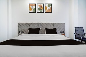 A modern hotel room with a large bed, a headboard with a geometric pattern, and three framed artworks on the wall.