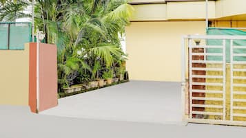 A gated entrance with a concrete pathway leading to a building with a yellow wall and a green fence.