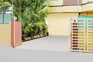 Uma entrada fechada com um caminho de concreto que leva a um edifício com parede amarela e cerca verde.