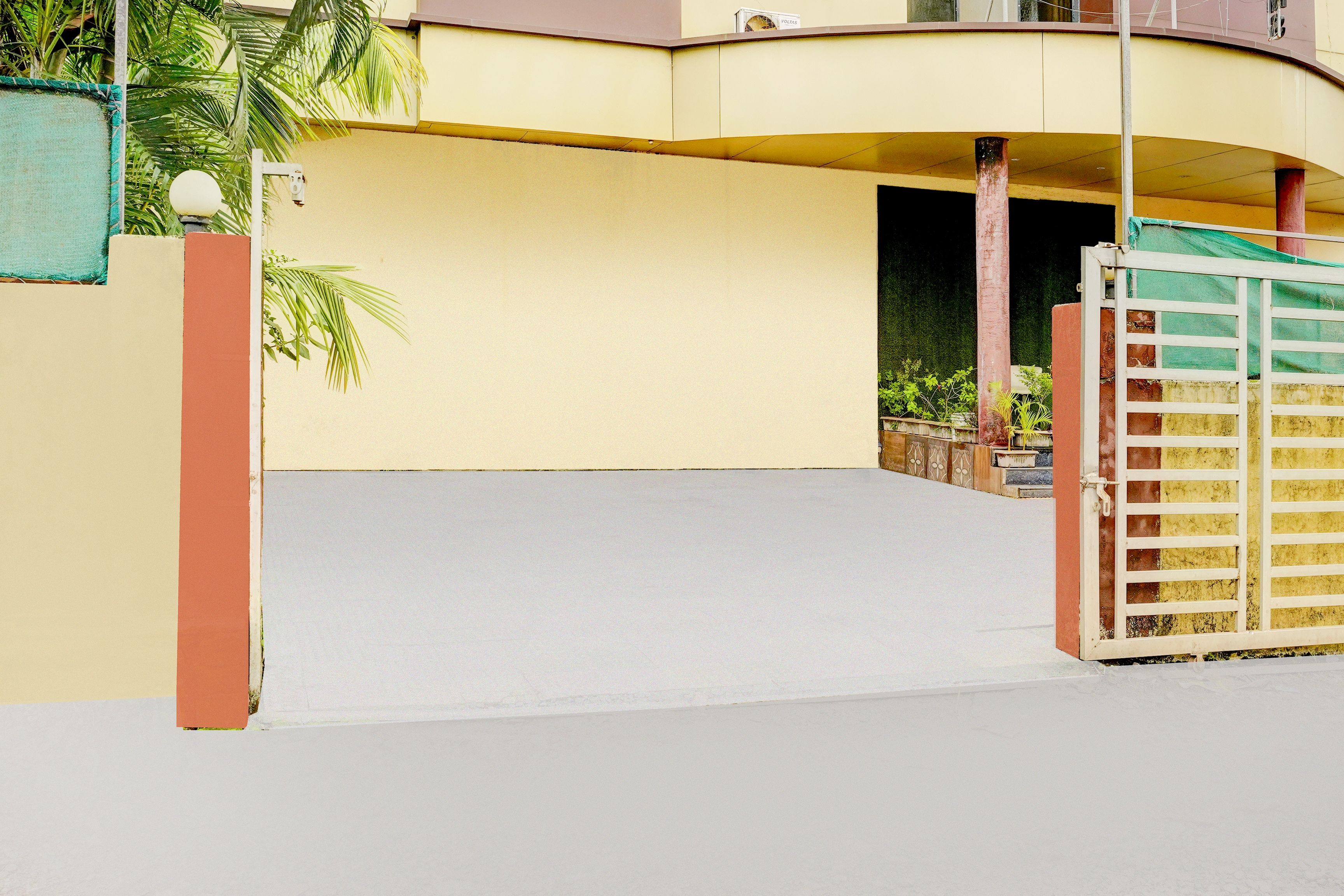 A residential building with a gated entrance, a paved driveway, and a small garden area.