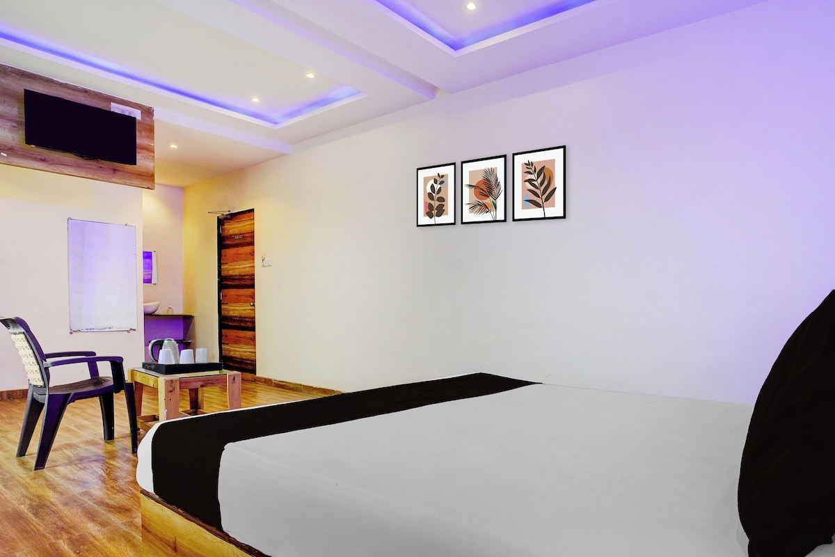A hotel room with a bed, a desk with a chair, a whiteboard, and three framed artworks on the wall.