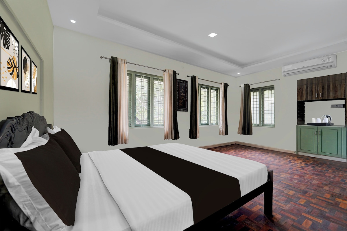 Una habitación de hotel con una cama, dos ventanas con cortinas, una kitchenette pequeña y obras de arte en la pared.