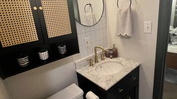 A bathroom with a toilet, sink, vanity, mirror, and towel rack.