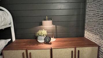 A bedroom with a wooden bed, a bedside table with a clock, a small plant, and a wall-mounted rack.