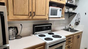 A kitchen with wooden cabinets, a microwave, a stove, a coffee maker, and a sink.