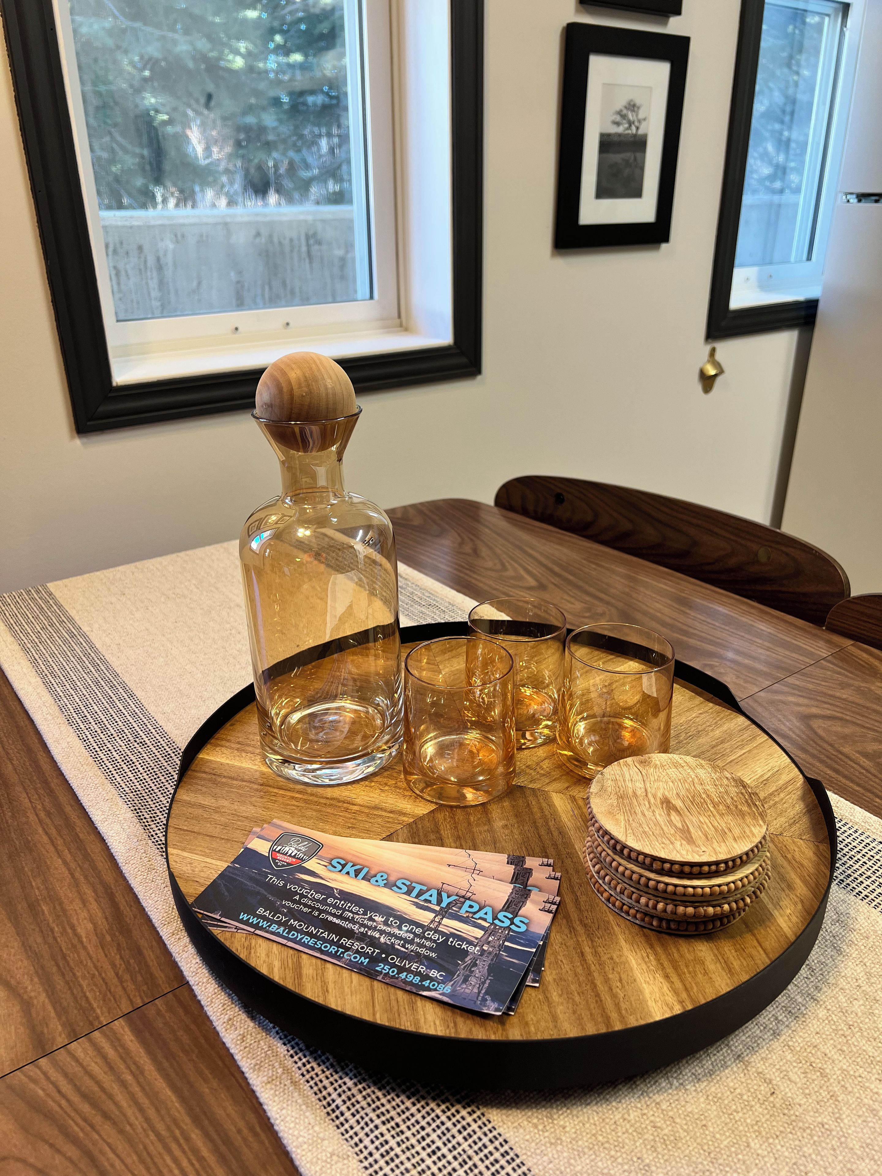 Ein Holztablett mit einer Flasche, Gläsern und einem Untersetzer auf einem Tisch.
