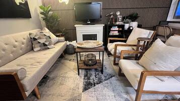 A modern living room with a sofa, armchairs, a coffee table, a television, and a fireplace.