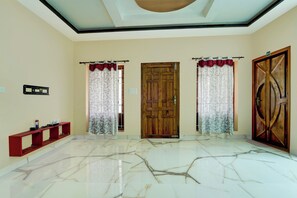 A room with a wooden door, two windows with curtains, a red console table, and a marble floor. - Hotel O NIMS Hospital (Neyyattinkara)
