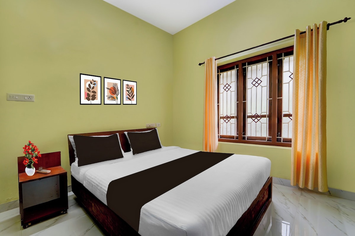 Habitación de hotel con cama, mesita de noche, un jarrón con flores y una ventana con cortinas.