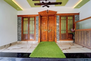 A foyer with a wooden double door, a ceiling fan, and a green artificial grass entrance mat. - Hotel O NIMS Hospital (Neyyattinkara)