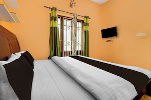 A hotel room with a bed, curtains, a television, and a window with a decorative metal gate.