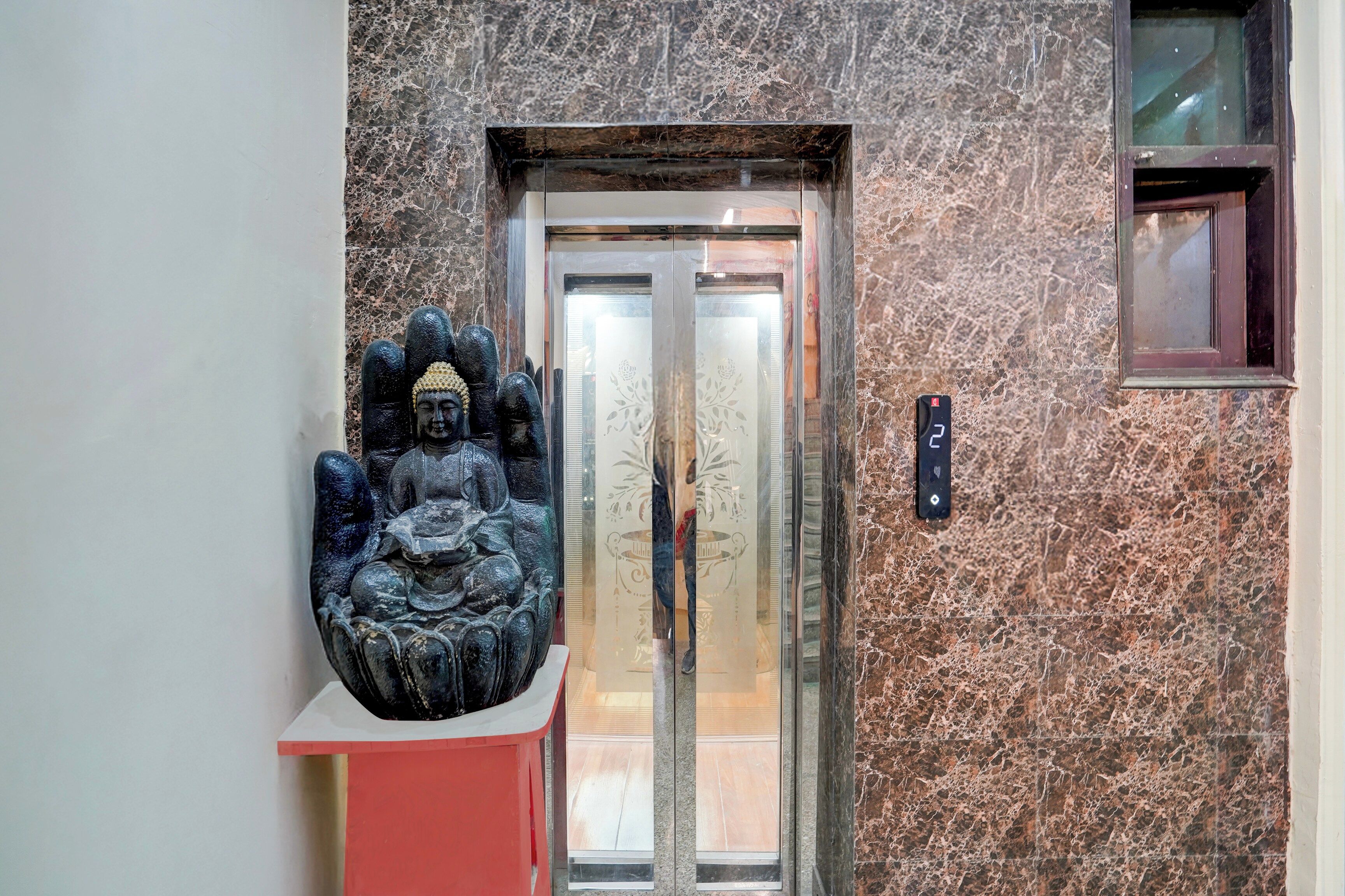 Una estatua de una figura sentada sobre un pedestal, una puerta de ascensor y una pared con textura.