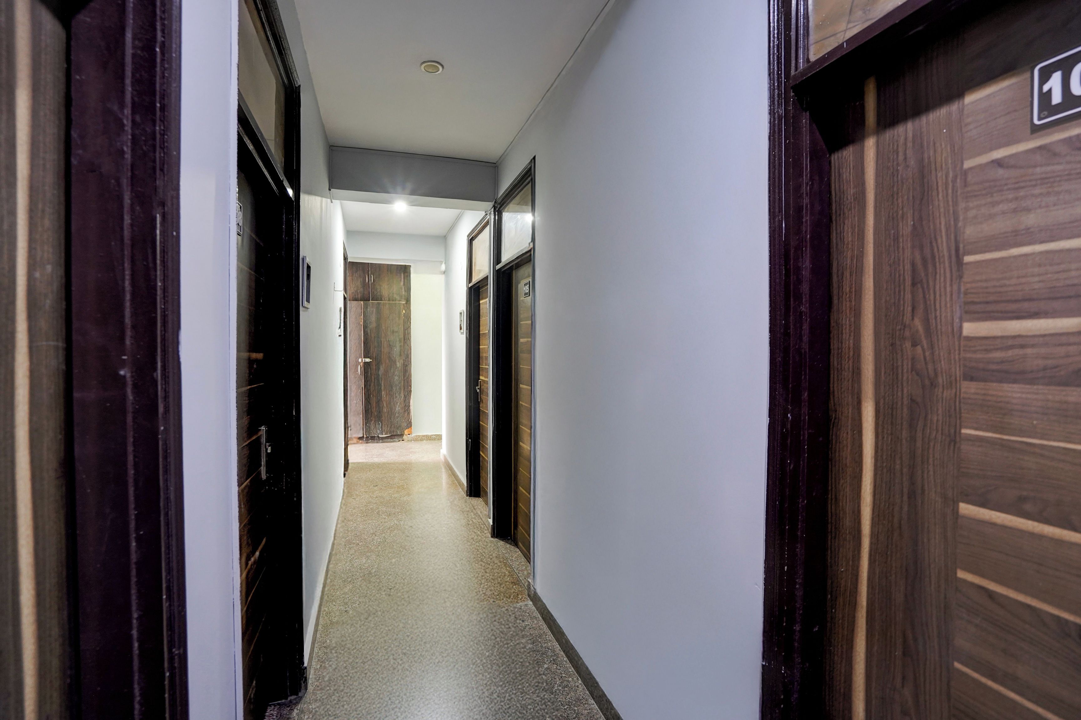 A corridor with doors on both sides, leading to a room with a wooden floor and a white wall.