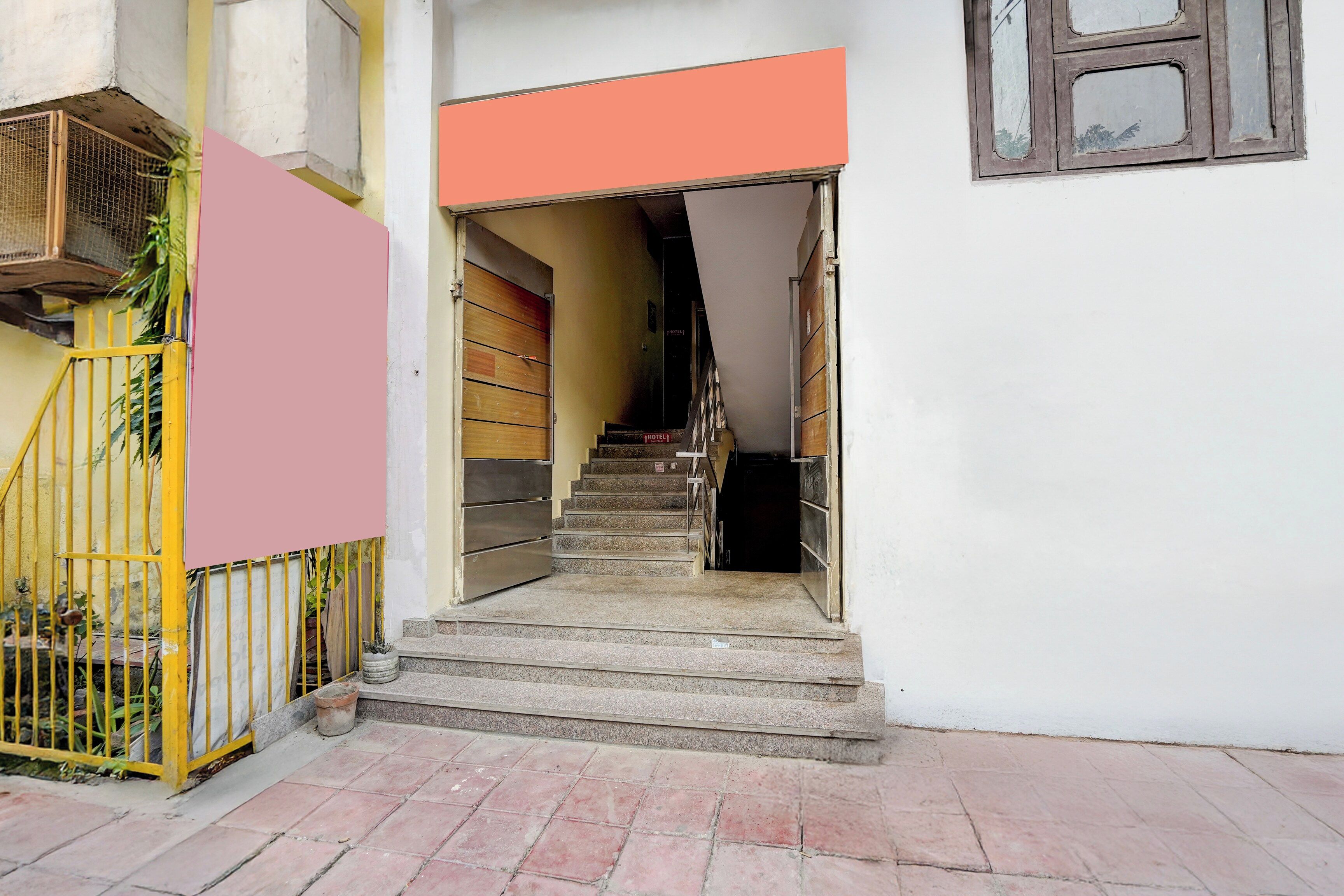 Eine Treppe führt zu einem Raum mit einer geschlossenen Tür, einem Fenster mit einem Metallgitter und einem gelben Tor mit einer Pflanze.