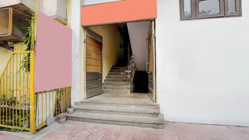 Eine Treppe führt zu einem Raum mit einer geschlossenen Tür, einem Fenster mit einem Metallgitter und einem gelben Tor mit einer Pflanze.