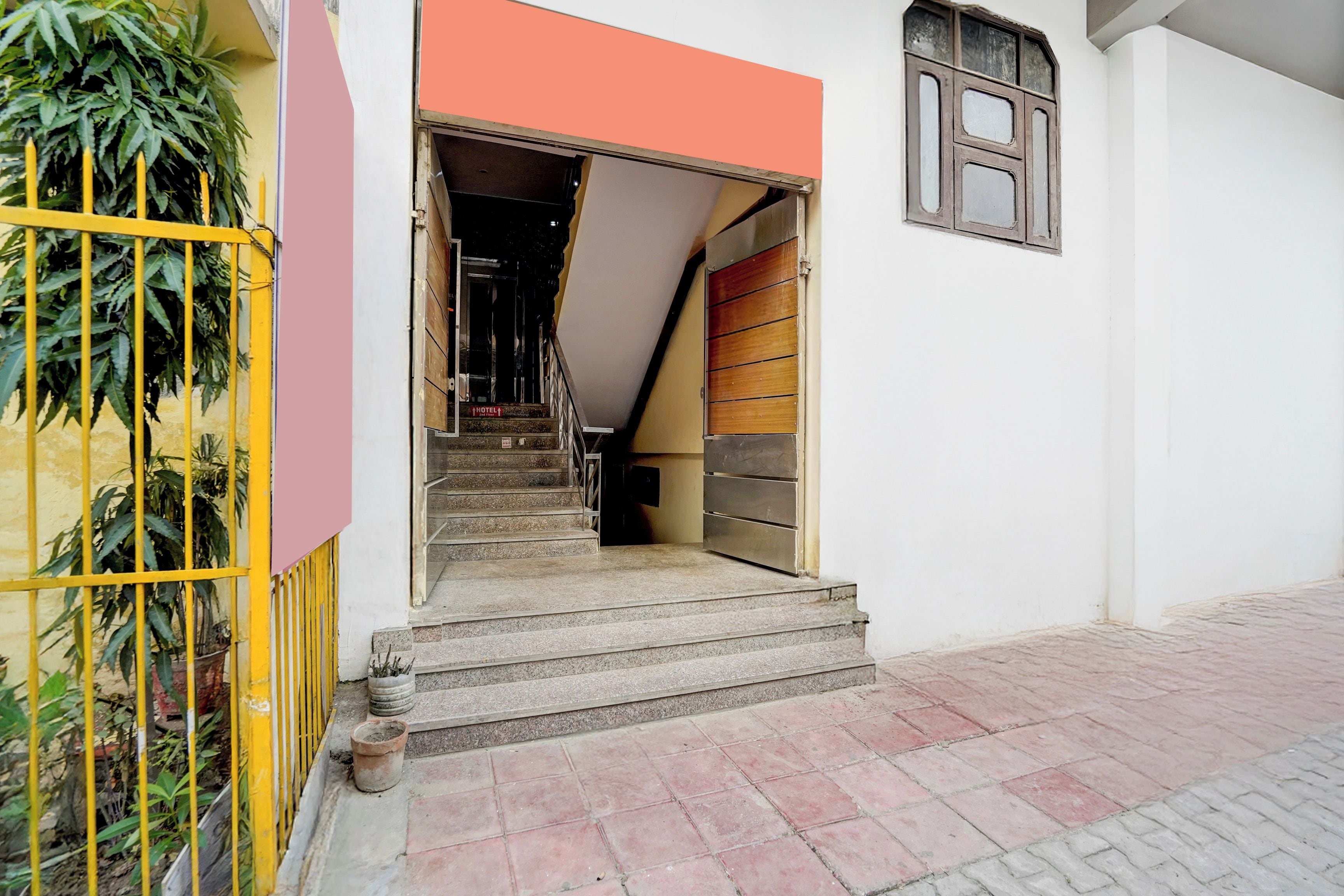 Una escalera conduce a la entrada de un hotel, con una reja metálica a la izquierda y una ventana a la derecha.