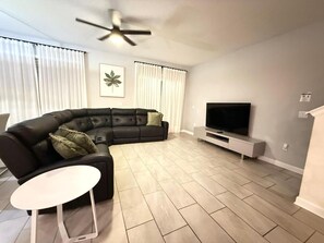 A living room with a sectional sofa, a flat-screen TV, a ceiling fan, and a small white table. - LUXURY 5BR PRIVATE POOL 8 MIN TO DISNEY SLEEPS 13 (Kissimmee)