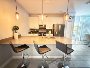 A modern kitchen with a central island, three bar stools, stainless steel appliances, and pendant lighting. - LUXURY 5BR PRIVATE POOL 8 MIN TO DISNEY SLEEPS 13 (Kissimmee)
