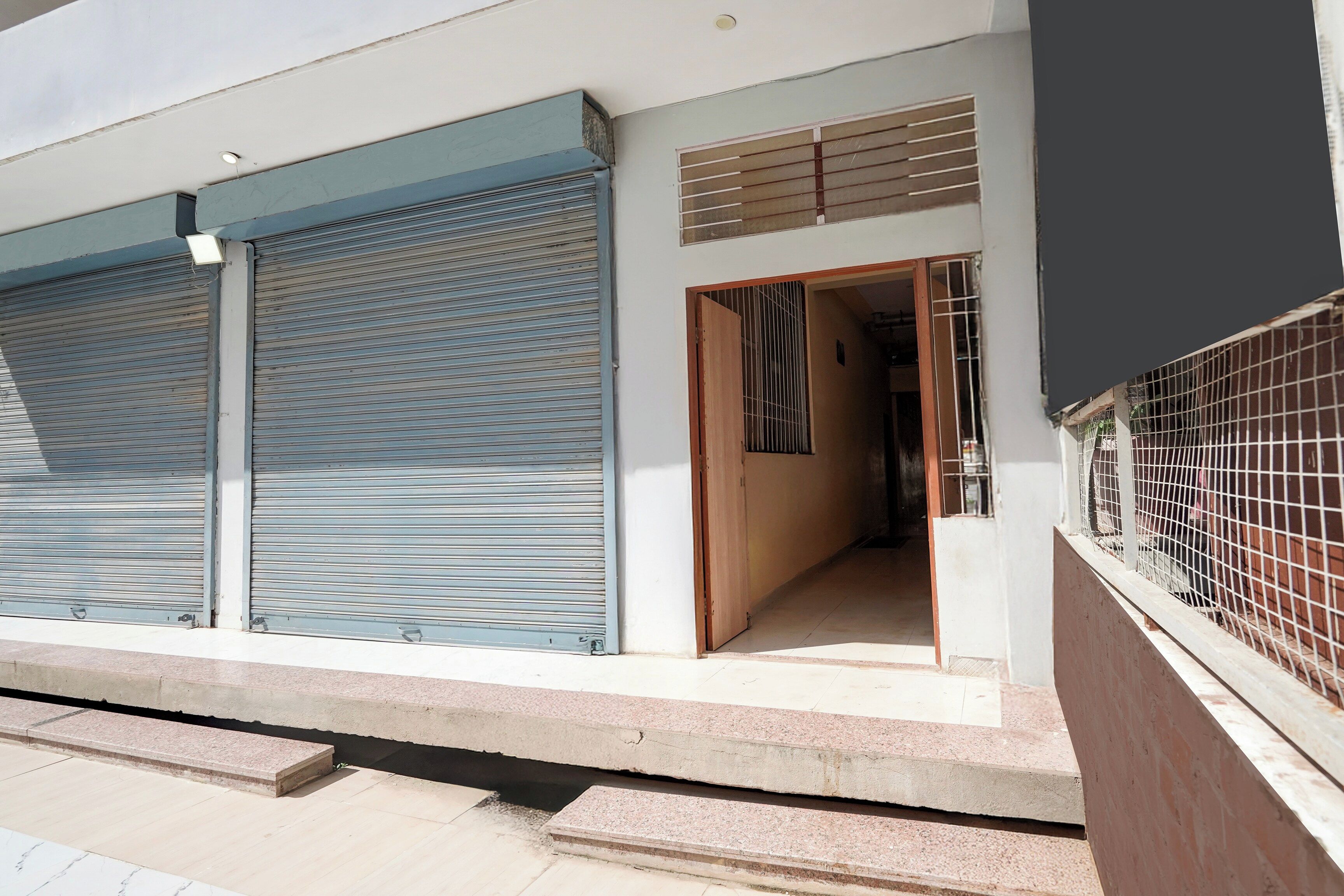A building with closed roller shutters, a visible entrance, and a gated area.