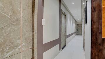 Un pasillo con suelo de mármol, una puerta de madera y una pared blanca con un interruptor de luz.