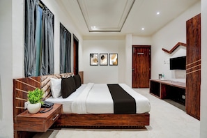 A modern bedroom with a large bed, a bedside table with a phone, a plant, and a wooden headboard.