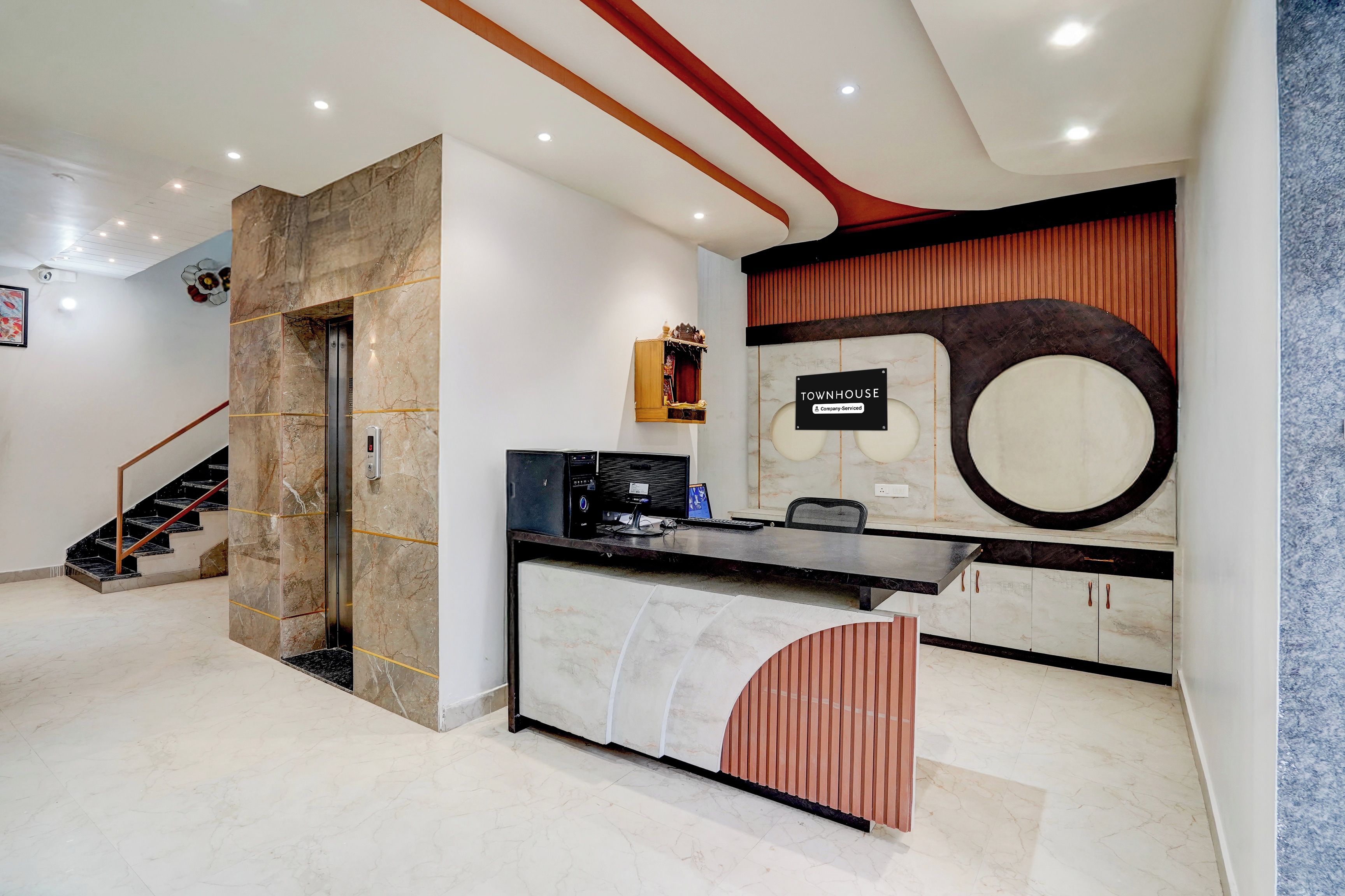 Ein moderner Empfangsbereich mit einer Marmortreppe, einem Empfischkiosk und einem Schild mit der Aufschrift 'TOWNHOUSE Company-Serviced'.