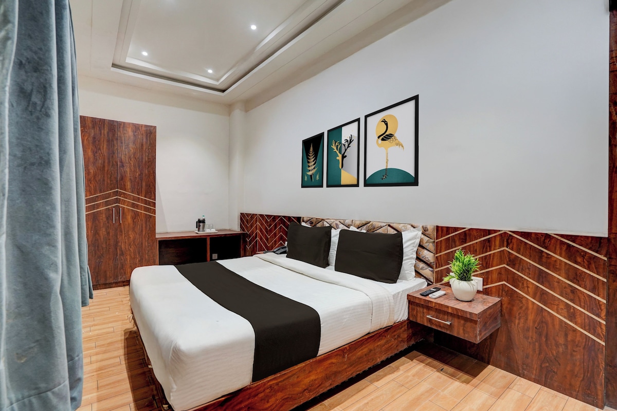 A hotel room with a bed, bedside table, nightstand, and a wall-mounted artwork.
