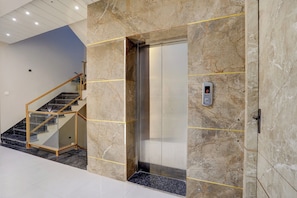 An elevator with a digital display, a marble wall, and a staircase with a glass railing.