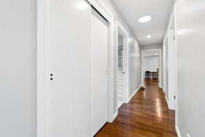 Passadís amb parets blanques i terra de fusta que condueix a una habitació amb escriptori i cadira.