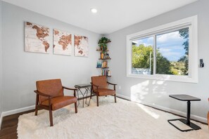 A room with two brown leather chairs, a small table, a bookshelf, a large window with a view, and three world map artworks on the wall. - Hillside Family Retreat · 3BR + Library · Near the Oakland Zoo (Oakland)