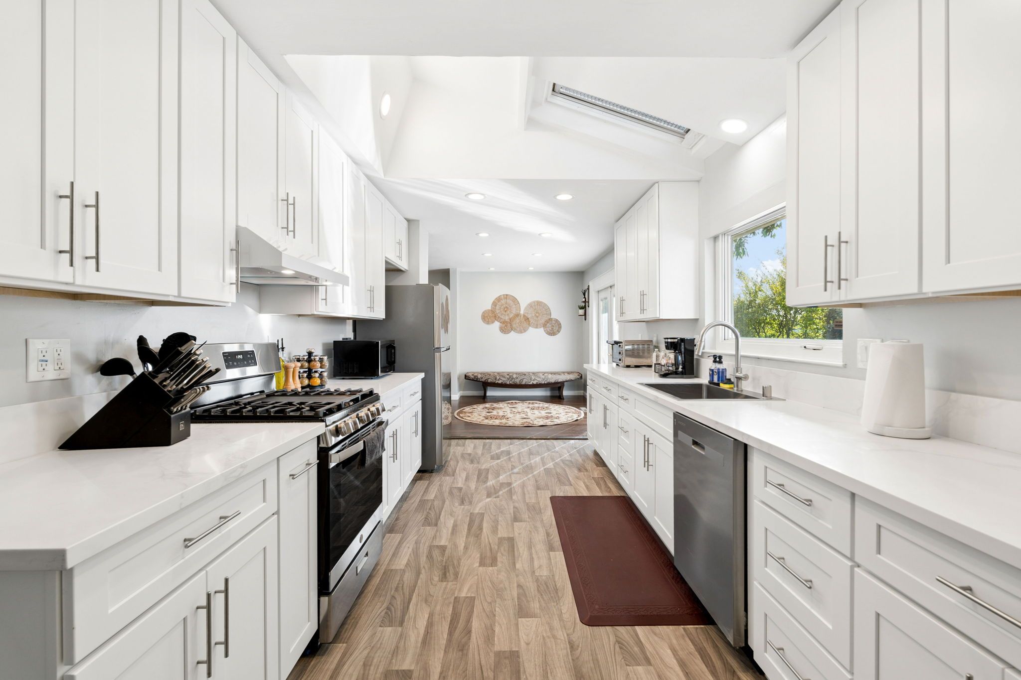 A modern kitchen with white cabinetry, a central island, and a view to the living area.