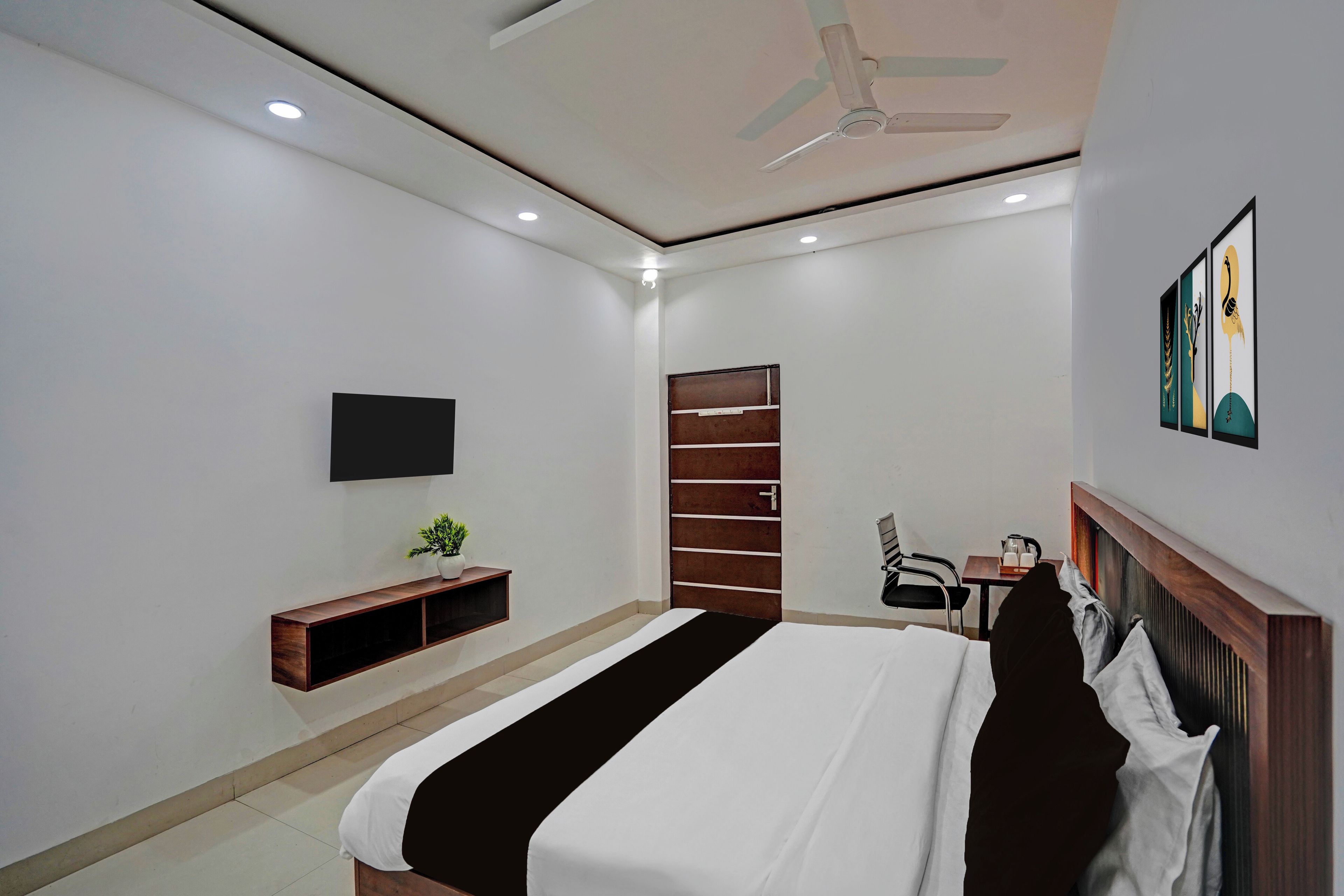 A hotel room with a bed, a desk, a chair, a TV mounted on the wall, and a ceiling fan.