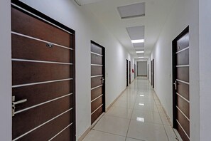A hotel corridor with wooden doors, white walls, and a tiled floor. - Hotel O Sector 110 Noida (Noida)