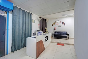 A reception desk with a 'RECEPTION' sign, a black sofa, a clock, and a fire extinguisher on the wall. - Hotel O Sector 110 Noida (Noida)