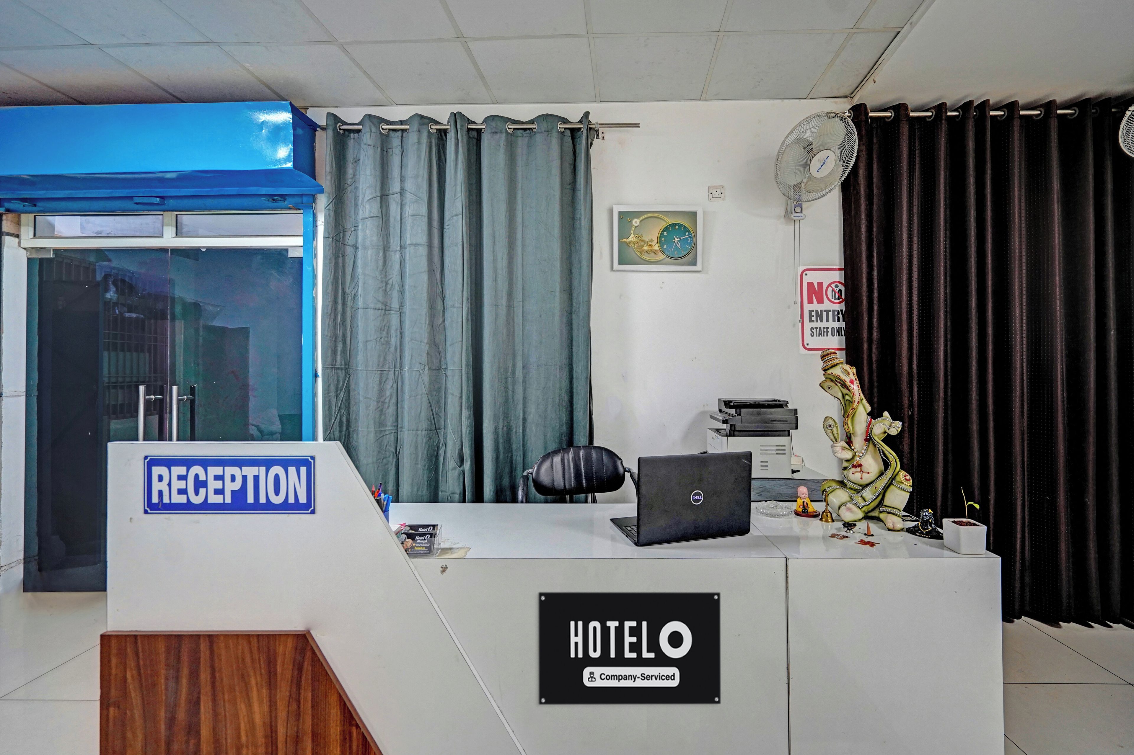 Una recepción de hotel con un letrero de recepción, un reloj, un cartel de 'No Entrar' y un ventilador en la pared.