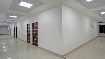 Um corredor longo e vazio, com paredes brancas, piso ladrilhado e várias portas de um lado.