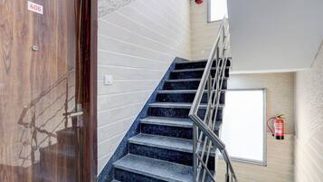 A staircase with a metal railing, a fire extinguisher mounted on the wall, and a door with a number sign.