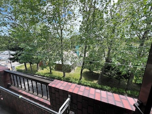 A view from a balcony with a brick wall, metal railing, and trees in the background. - Beautiful parkview 3-bedroom condo with AC/WiFi in Hokkaido's capital Sapporo (Sapporo)