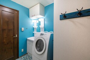 Ein kleiner Hauswirtschaftsraum mit einer Waschmaschine, einem Schrank darüber und einem Wandregal mit Dekoration.