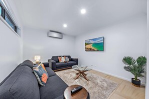Ein modernes Wohnzimmer mit einer Couch, einem Couchtisch, einem Gemälde vom Strand und einer Topfpflanze.