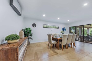A dining area with a wooden table and chairs, a potted plant, and a wall-mounted clock. - Whitsunday Sanctuary Retreat - Mountain Views (Jubilee Pocket)