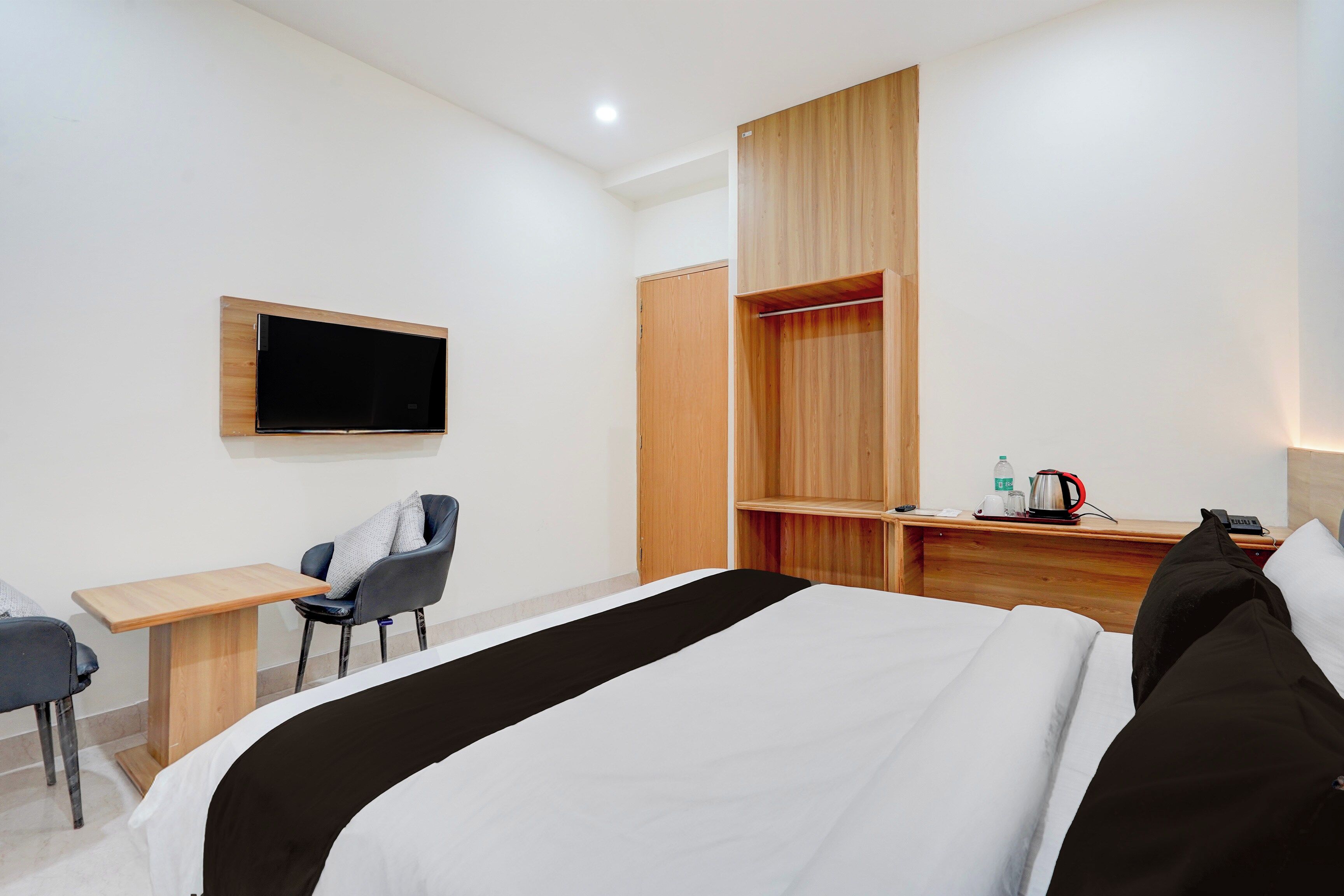 A hotel room with a bed, a desk, a chair, a TV mounted on the wall, and a wardrobe.