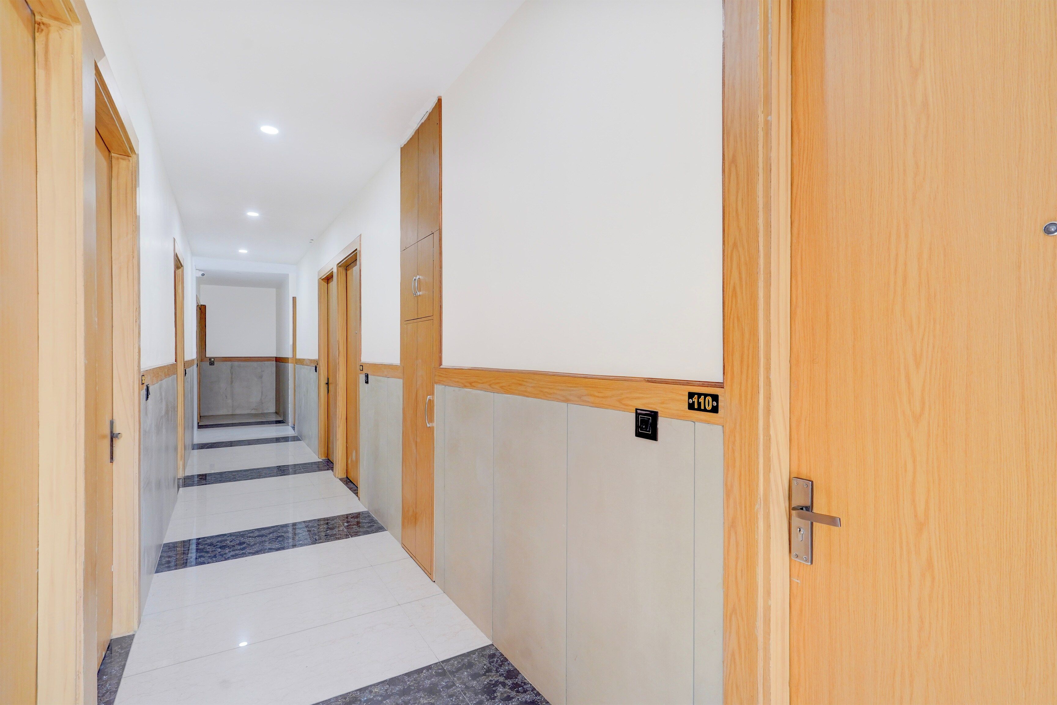 A corridor with wooden doors, numbered room signs, and a tiled floor.