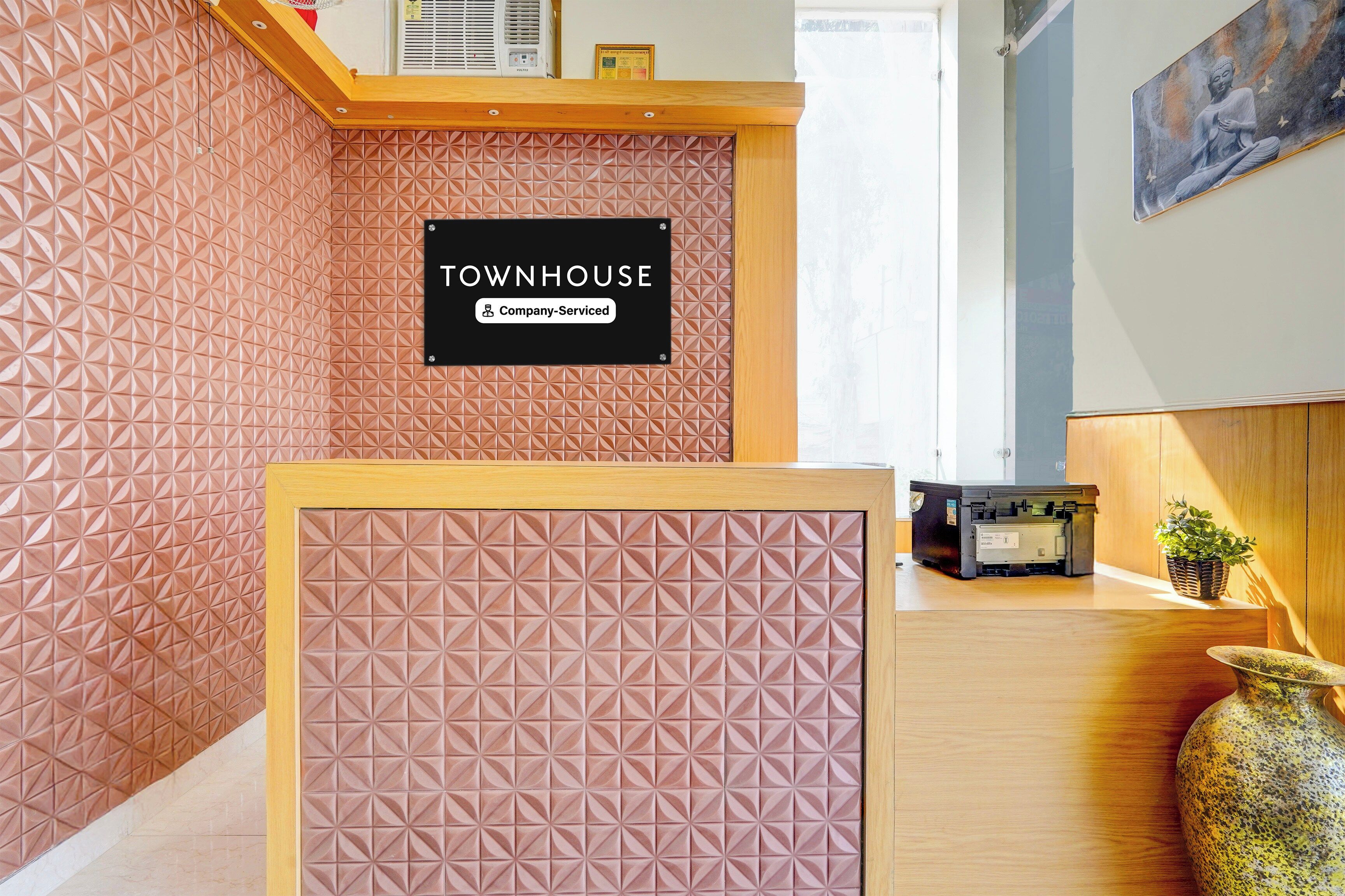 Un comptoir d’accueil avec un mur orné d’un motif géométrique, une enseigne indiquant « TOWNHOUSE, services d’entreprise », et une imprimante posée sur le comptoir.
