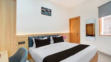 Habitación de hotel con cama, escritorio, silla, espejo y un cuadro en la pared.