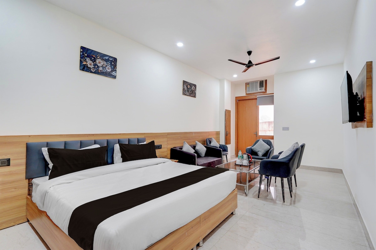 A modern hotel room with a large bed, a seating area with chairs, a ceiling fan, and artwork on the walls.