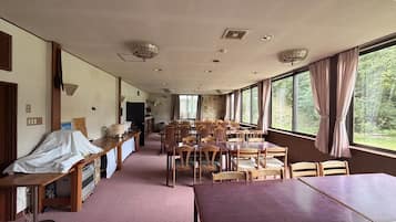 A dining area with tables and chairs, a counter with a cash register, and a view of the outdoors through large windows.
