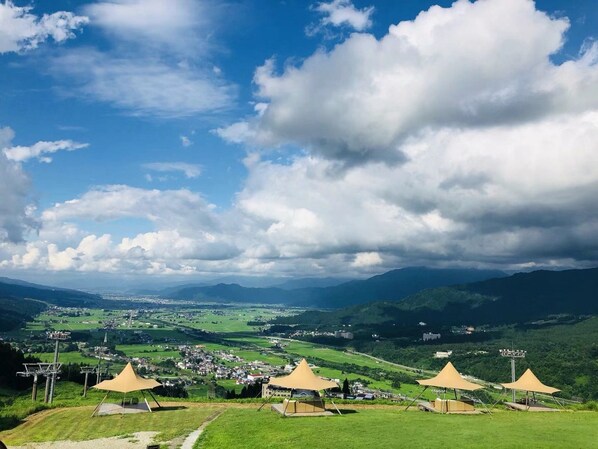 Une vue panoramique d’un paysage montagneux avec un village en contrebas, où l’on aperçoit plusieurs grandes tentes et un ciel dégagé.