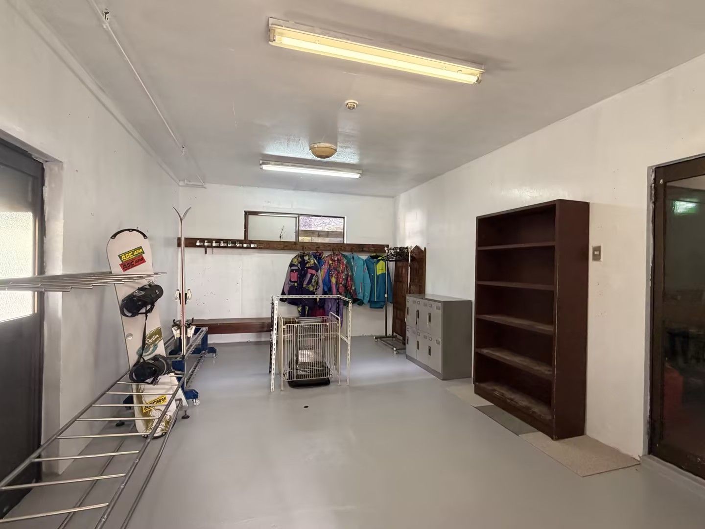 A hallway with a metal rack holding helmets and a bicycle, a clothing rack with colorful jackets, and a large cabinet with multiple drawers.
